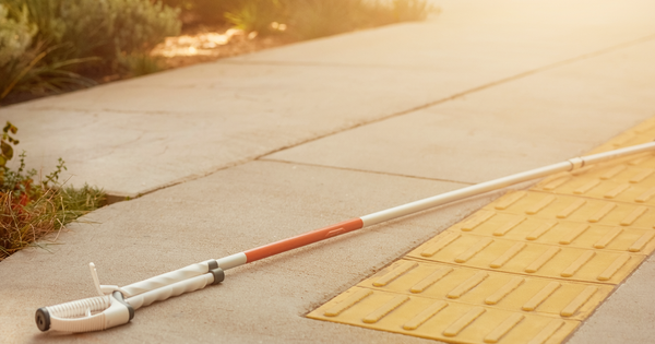Illustrative photograph of a white mobility cane and tactile pedestrian paving
