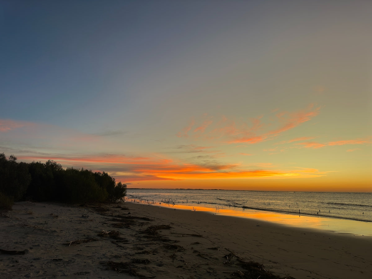The sunset colors the sky over a calm beach.
