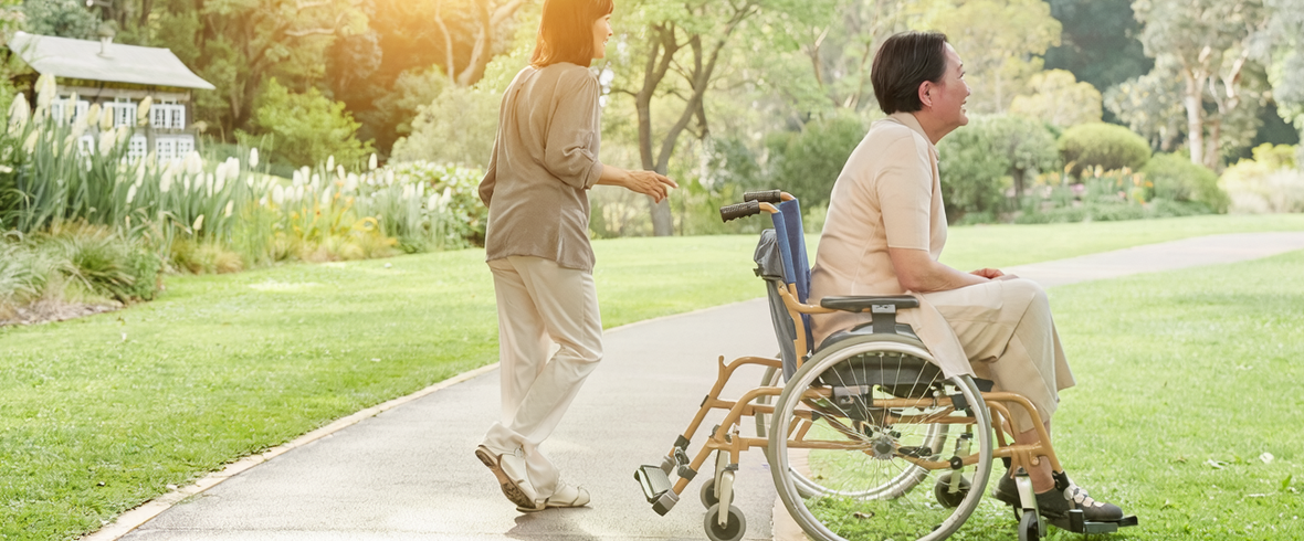 Illustrative photograph of a wheelchair user and supporter on a wide park path