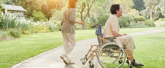 Illustrative photograph of a wheelchair user and supporter on a wide park path