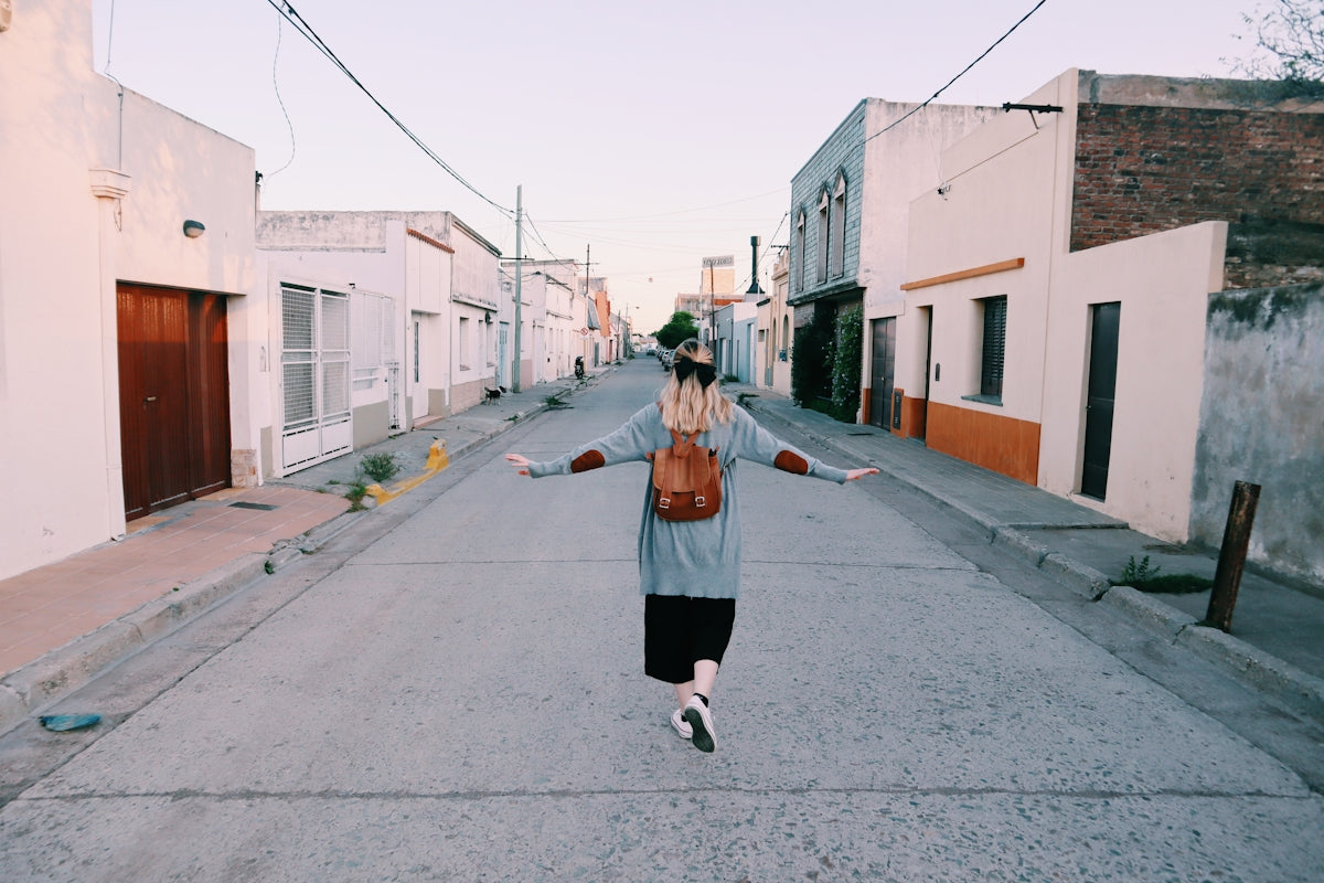 woman in brown coat and black pants walking on gray concrete road during daytime