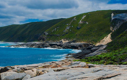 a rocky beach with a body of water and mountains in the background