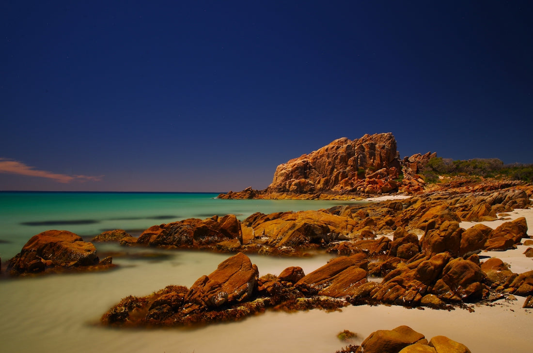 a beach with rocks and water under a blue sky