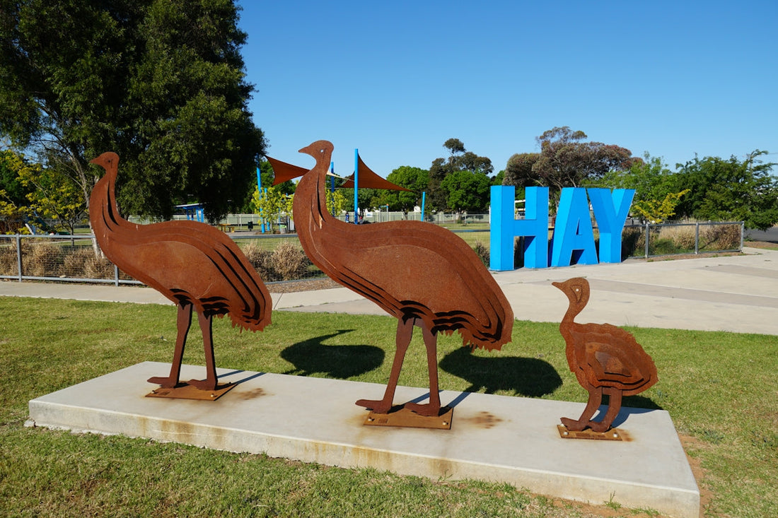 Rusty emu sculptures stand in hay.