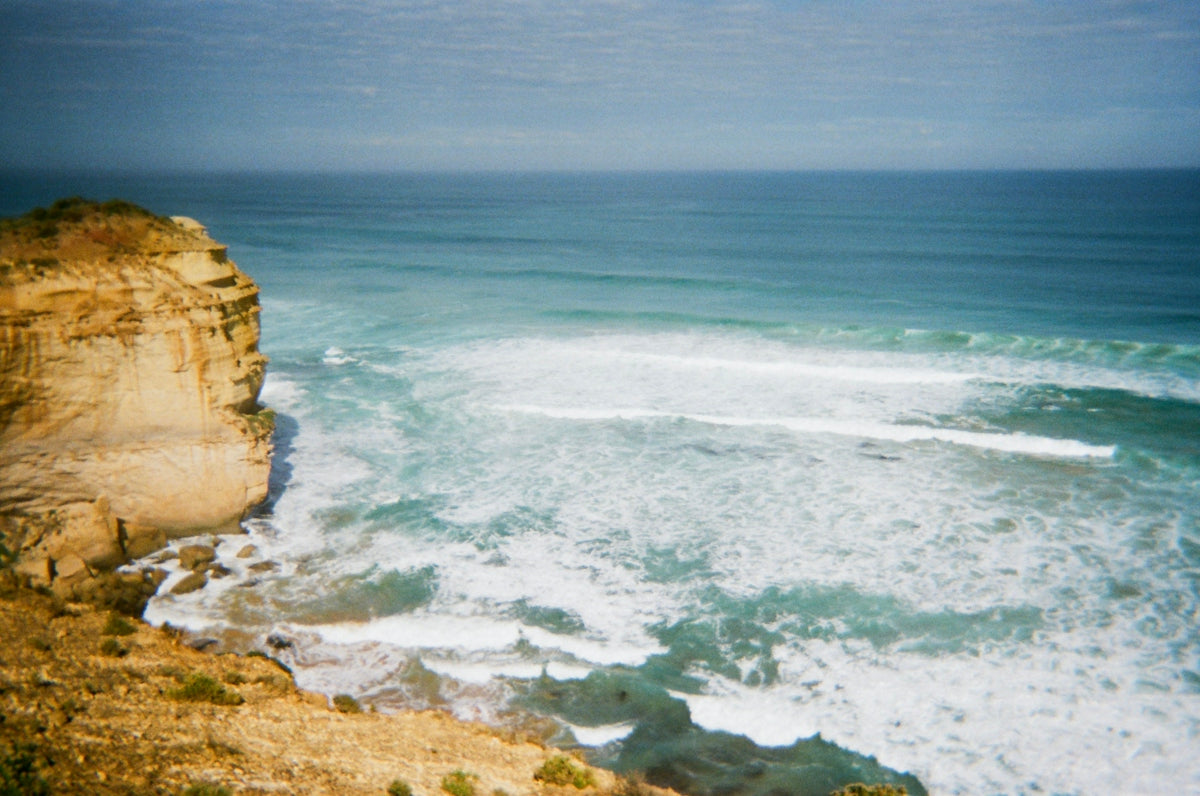 A rocky cliff overlooks the vast ocean with breaking waves