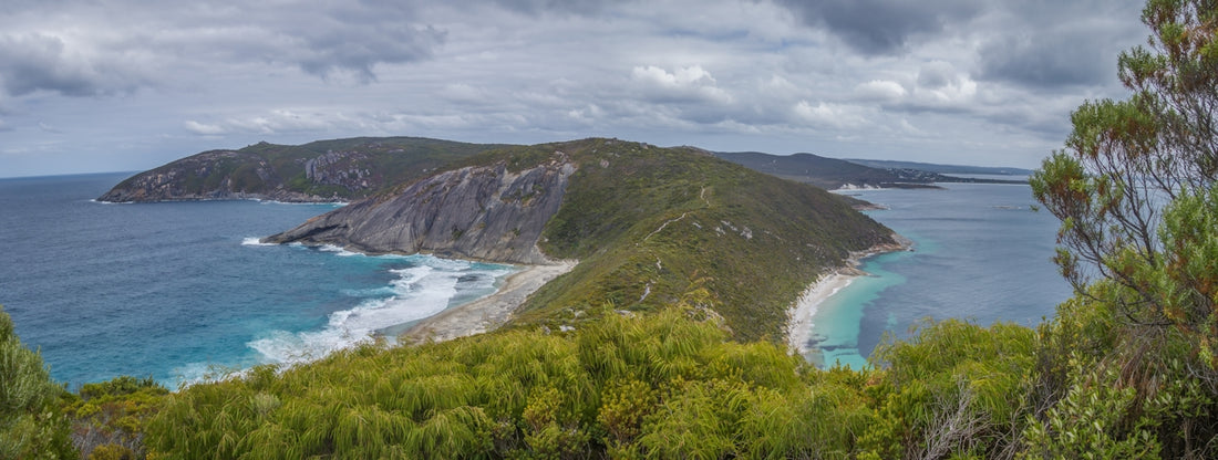 Panoramic coastal landscape with beaches, ocean, and green hills.
