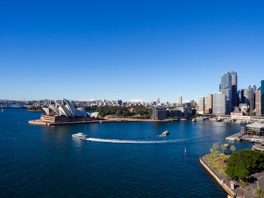Sydney harbour, opera house, cityscape, and boats under clear sky.